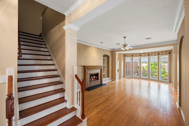 unfurnished living room featuring ceiling fan, ornate columns, ornamental molding, a premium fireplace, and light hardwood / wood-style floors