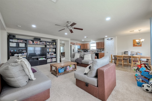 living room featuring ceiling fan with notable chandelier, a textured ceiling, and light carpet