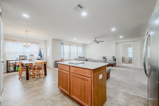 kitchen with hanging light fixtures, a textured ceiling, a center island, and stainless steel fridge