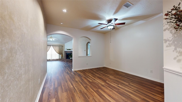 empty room featuring dark hardwood / wood-style flooring, ceiling fan, a fireplace, and a textured ceiling