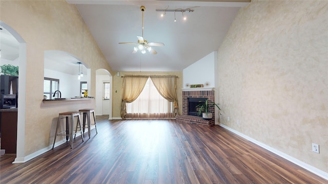 unfurnished living room featuring high vaulted ceiling, sink, dark hardwood / wood-style floors, ceiling fan, and a fireplace