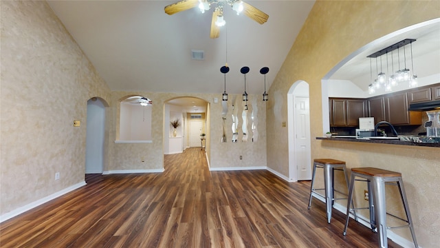 kitchen featuring dark hardwood / wood-style flooring, ceiling fan, decorative light fixtures, high vaulted ceiling, and a breakfast bar area