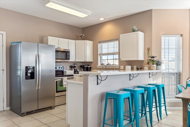 kitchen with stainless steel appliances, light tile patterned floors, a kitchen breakfast bar, kitchen peninsula, and white cabinets