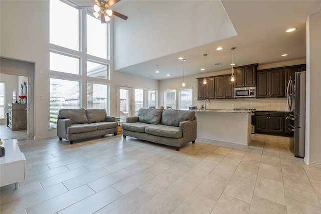 living room featuring a towering ceiling, ceiling fan, sink, and light tile patterned floors