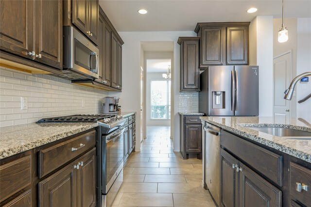 kitchen with stainless steel appliances, sink, light stone countertops, dark brown cabinets, and decorative backsplash