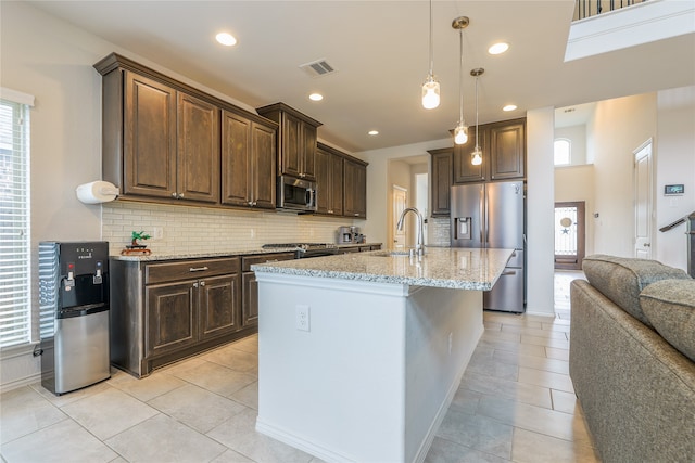 kitchen with stainless steel appliances, a center island with sink, sink, backsplash, and dark brown cabinets