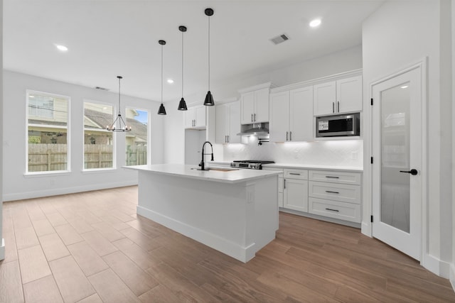 kitchen with light wood-type flooring, appliances with stainless steel finishes, an island with sink, and white cabinets