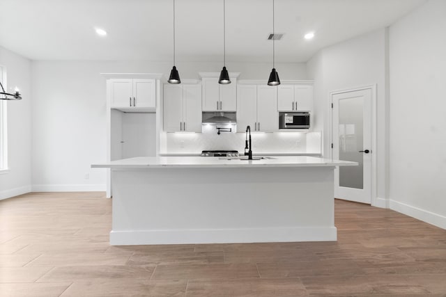 kitchen with white cabinetry, decorative light fixtures, light hardwood / wood-style floors, and a kitchen island with sink