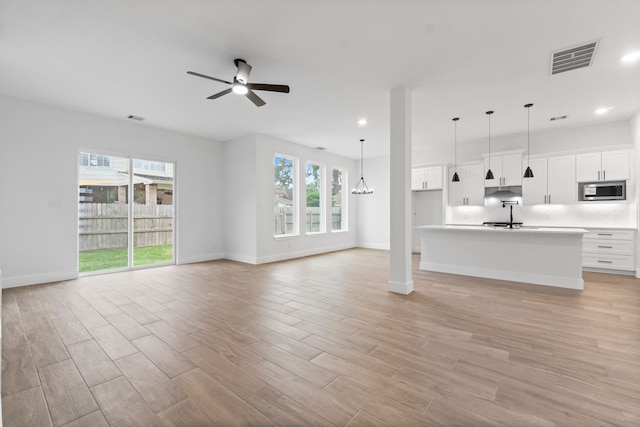 unfurnished living room featuring a wealth of natural light, ceiling fan with notable chandelier, and light wood-type flooring