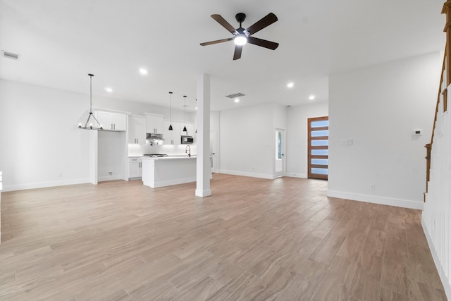 unfurnished living room with sink, ceiling fan with notable chandelier, and light hardwood / wood-style flooring