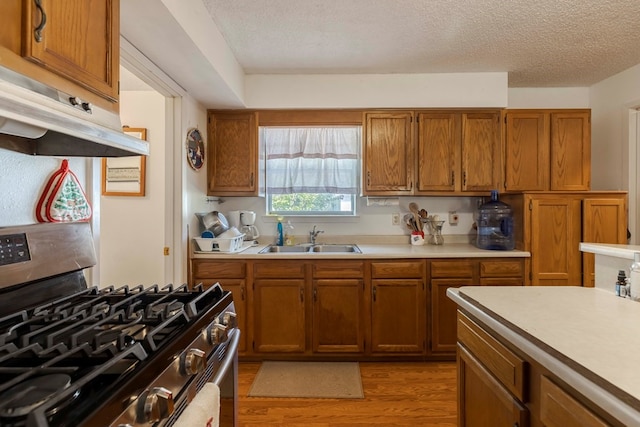 kitchen with a textured ceiling, stainless steel range with gas stovetop, sink, and light wood-type flooring