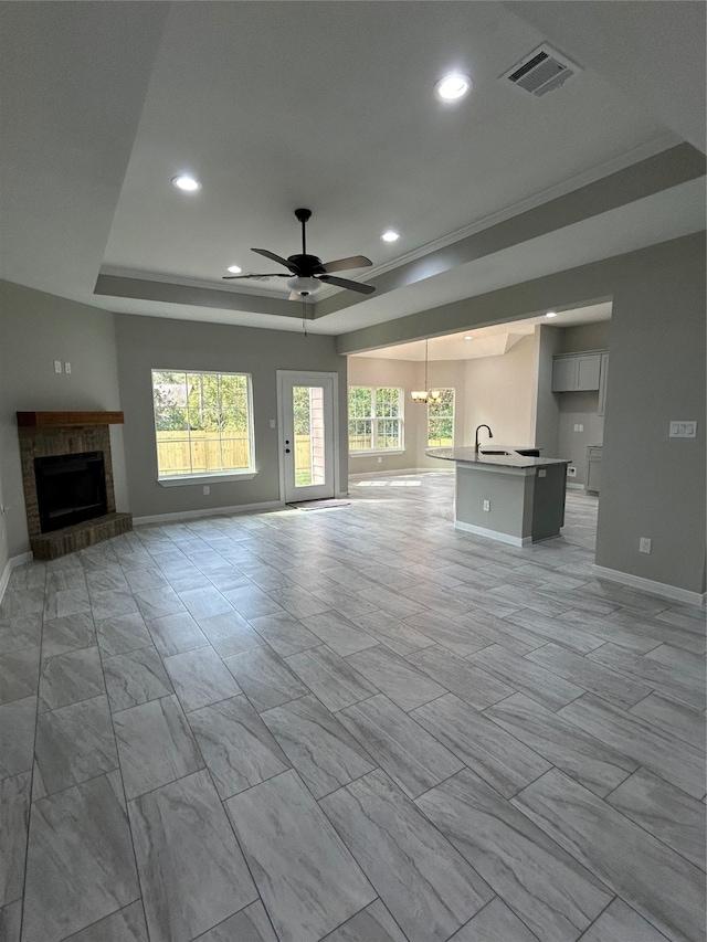 unfurnished living room with a fireplace, a tray ceiling, crown molding, and ceiling fan with notable chandelier