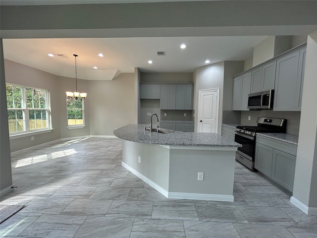 kitchen featuring light stone counters, a chandelier, sink, an island with sink, and appliances with stainless steel finishes