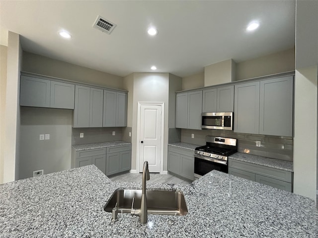 kitchen featuring gray cabinetry, light stone countertops, sink, and stainless steel appliances