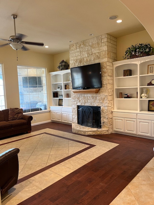 living room with a stone fireplace, ceiling fan, a wealth of natural light, and light hardwood / wood-style floors