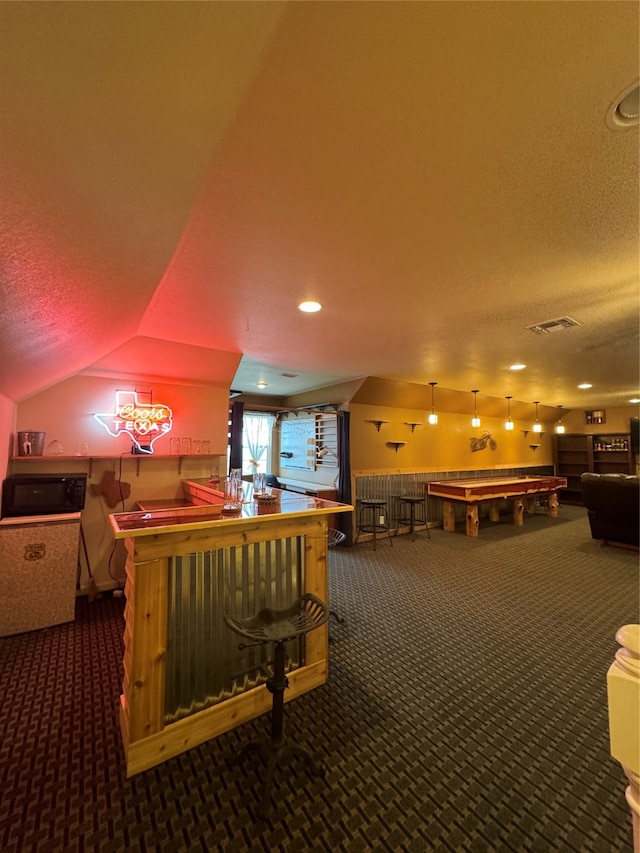 recreation room featuring bar, a textured ceiling, vaulted ceiling, and dark carpet