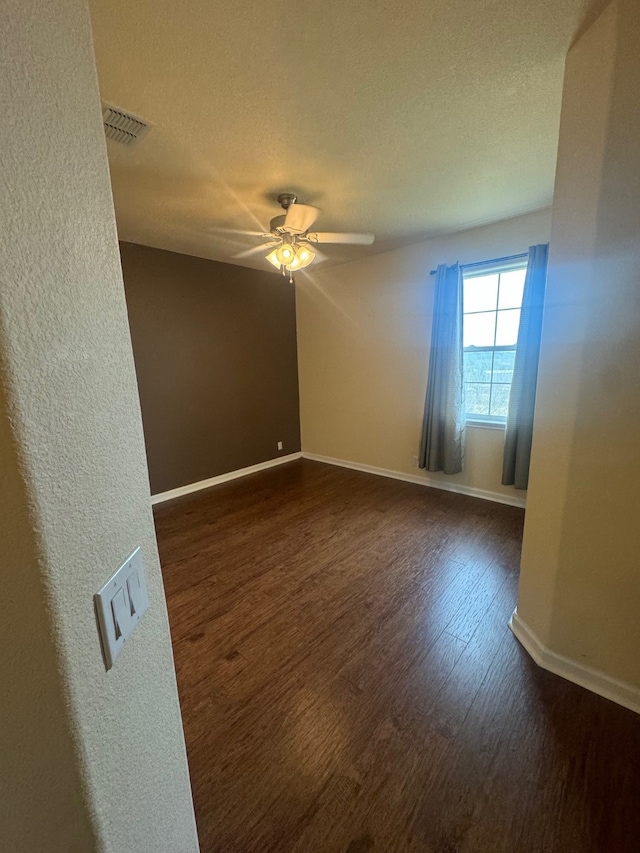 empty room featuring a textured ceiling, dark wood-type flooring, and ceiling fan