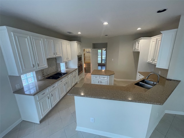 kitchen with decorative backsplash, sink, white cabinets, kitchen peninsula, and a center island