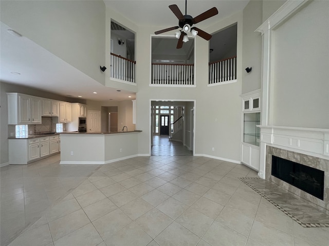 unfurnished living room with a tiled fireplace, light tile patterned floors, and a high ceiling