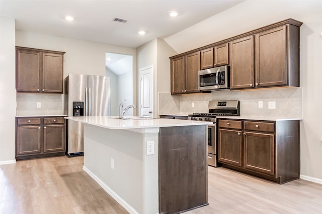 kitchen featuring decorative backsplash, appliances with stainless steel finishes, an island with sink, and light hardwood / wood-style flooring