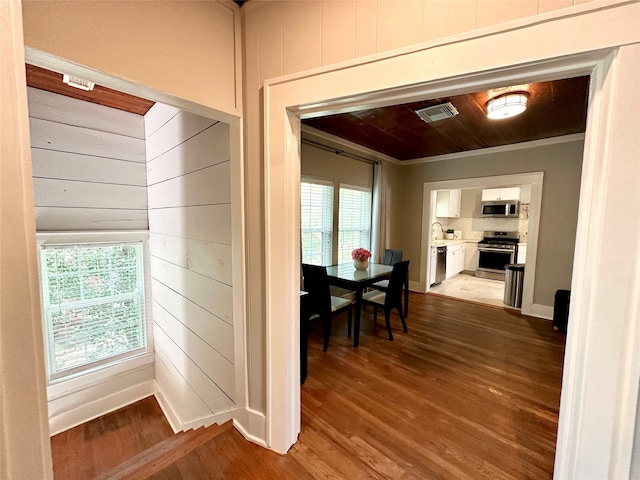 hallway with hardwood / wood-style floors, wooden walls, crown molding, and sink