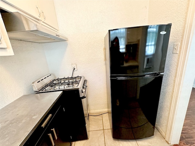 kitchen with white cabinets, black refrigerator, light tile patterned floors, and gas stove