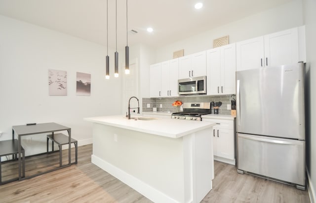 kitchen featuring stainless steel appliances, white cabinets, sink, an island with sink, and decorative light fixtures