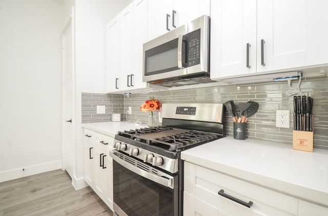 kitchen with decorative backsplash, white cabinetry, light wood-type flooring, and appliances with stainless steel finishes