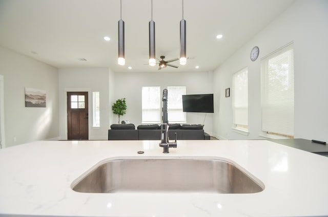 kitchen featuring light stone countertops, pendant lighting, sink, and ceiling fan