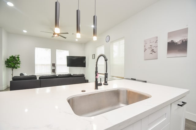 kitchen featuring white cabinets, hanging light fixtures, sink, and light stone countertops