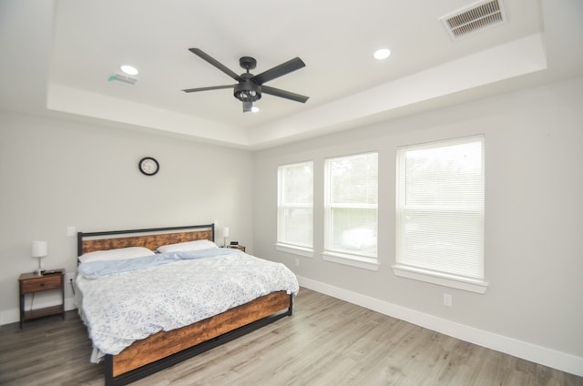 bedroom with light hardwood / wood-style floors, ceiling fan, and a raised ceiling