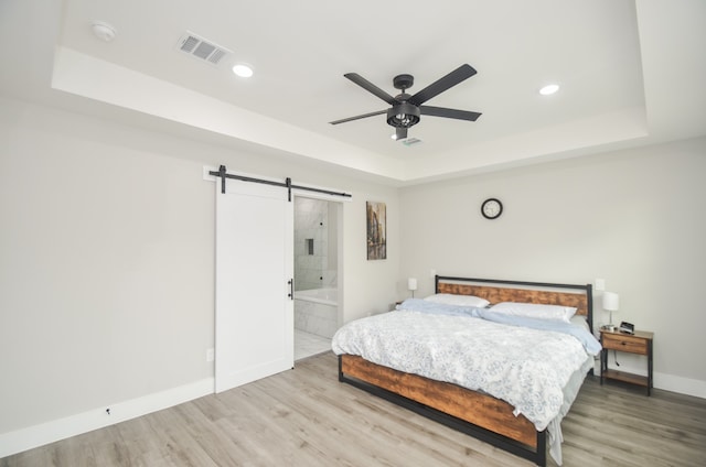 bedroom featuring wood-type flooring, a barn door, ceiling fan, and ensuite bathroom