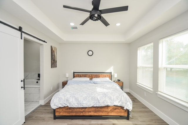 bedroom with hardwood / wood-style flooring, a barn door, ceiling fan, and connected bathroom