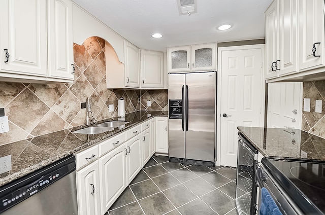 kitchen featuring white cabinetry, sink, appliances with stainless steel finishes, dark stone counters, and backsplash