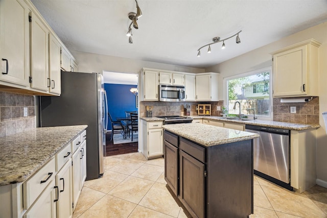 kitchen featuring appliances with stainless steel finishes, tasteful backsplash, light stone counters, sink, and a center island