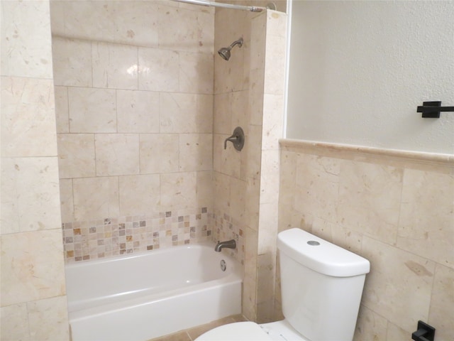 bathroom with toilet, tiled shower / bath combo, and tile walls