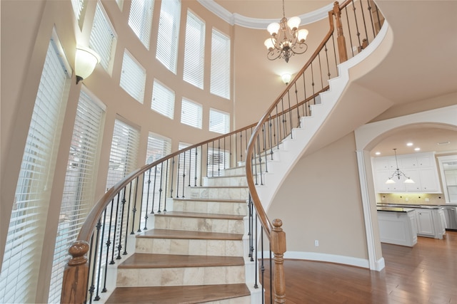 staircase featuring crown molding, hardwood / wood-style floors, a notable chandelier, and a high ceiling