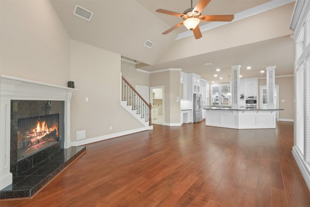 unfurnished living room with high vaulted ceiling, a tiled fireplace, dark wood-type flooring, and decorative columns