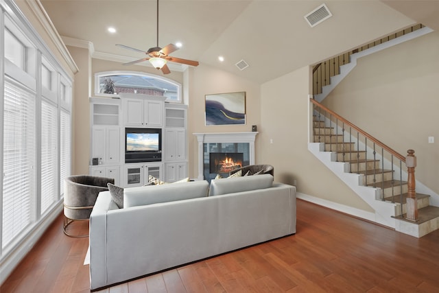 living room with wood-type flooring, a tile fireplace, high vaulted ceiling, and crown molding