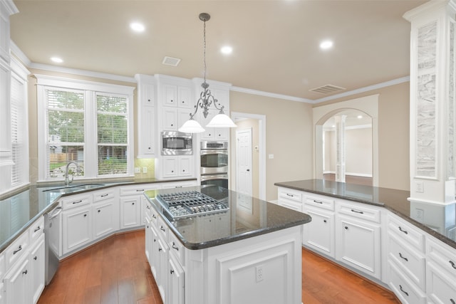 kitchen with wood-type flooring, appliances with stainless steel finishes, hanging light fixtures, white cabinets, and a center island