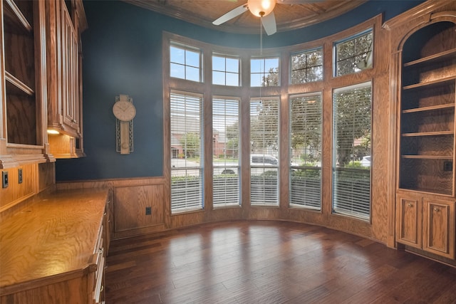 unfurnished dining area with built in shelves, wooden walls, dark hardwood / wood-style floors, and ceiling fan