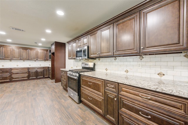 kitchen with decorative backsplash, stainless steel appliances, dark hardwood / wood-style floors, and light stone countertops