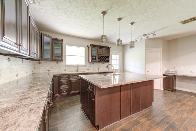 kitchen featuring pendant lighting, dark hardwood / wood-style flooring, sink, and an island with sink