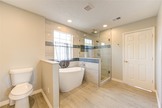 bathroom with toilet, a textured ceiling, and separate shower and tub