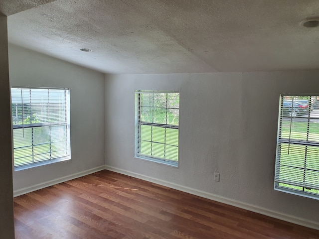 spare room with vaulted ceiling, hardwood / wood-style flooring, and a textured ceiling