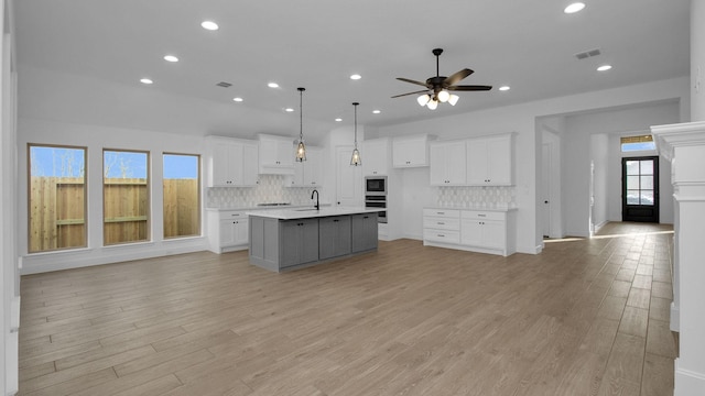 kitchen featuring light countertops, an island with sink, white cabinetry, and decorative light fixtures