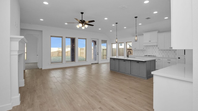 kitchen featuring white cabinets, an island with sink, open floor plan, hanging light fixtures, and light countertops