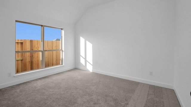 carpeted empty room with a wealth of natural light, vaulted ceiling, and baseboards