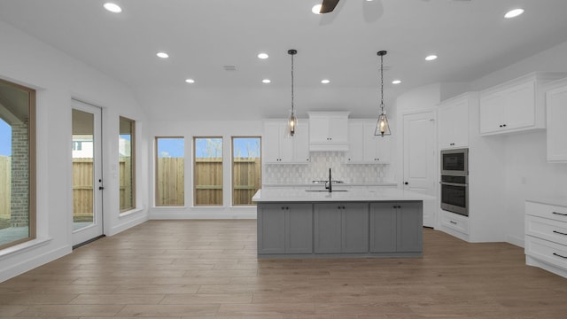 kitchen with light countertops, decorative light fixtures, a kitchen island with sink, and white cabinets