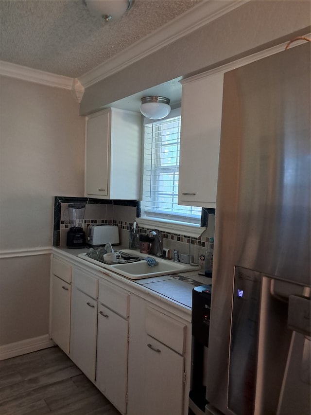 kitchen with white cabinets, stainless steel fridge with ice dispenser, tasteful backsplash, and crown molding